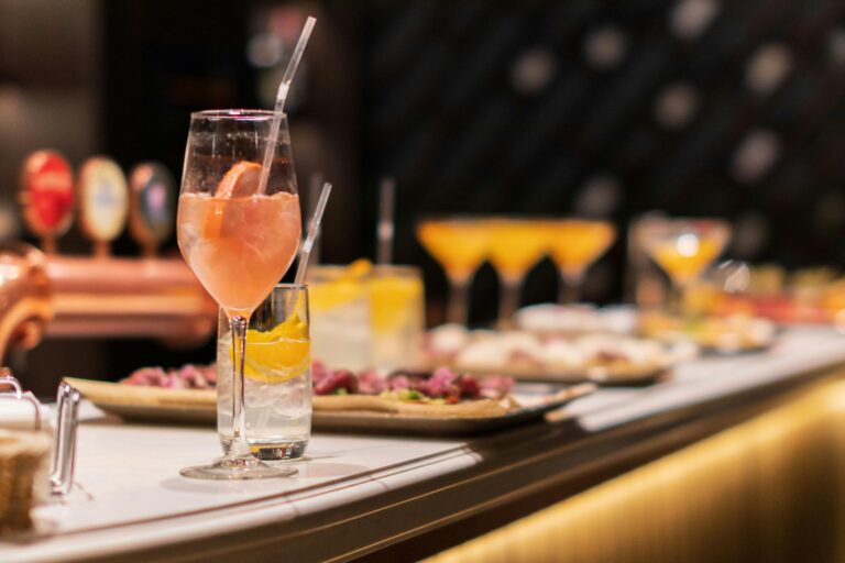 Vibrant cocktails and appetizers lined up elegantly on a bar counter in a stylish setting.